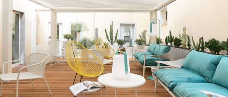 An outdoor patio with white and yellow chairs, a turquoise sofa, and various potted plants.