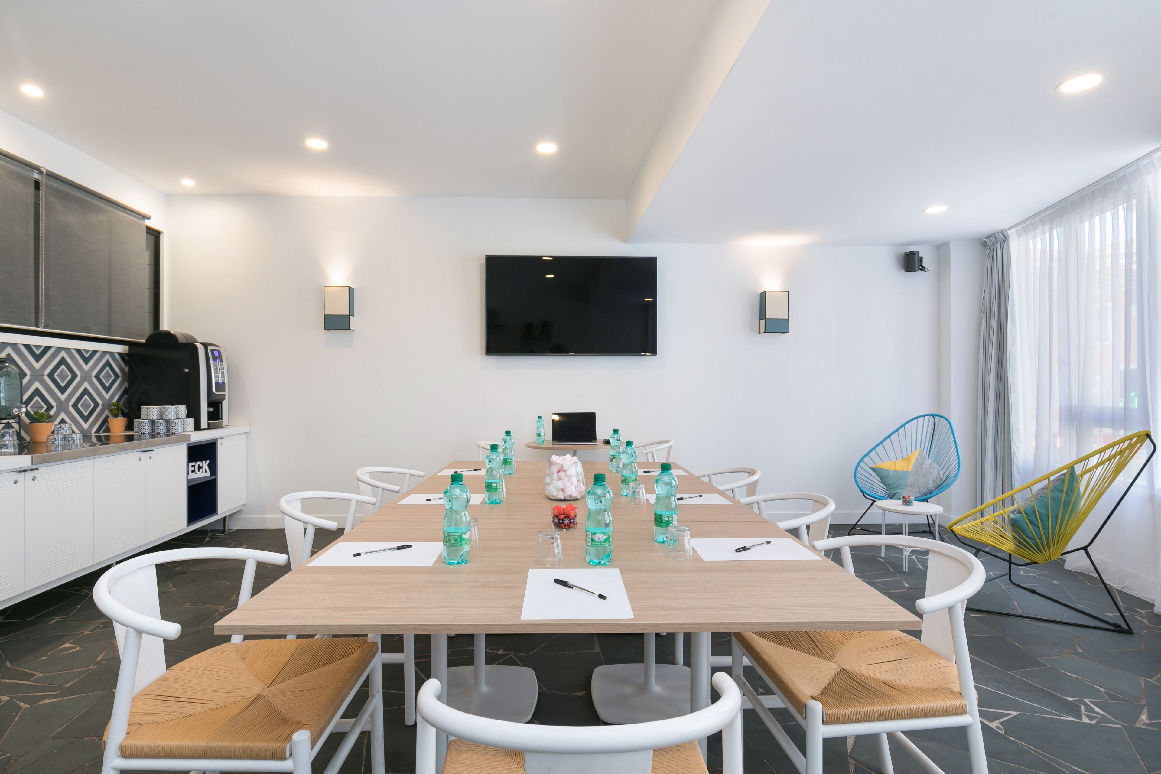 A modern conference room with a long table, white chairs, and a flat-screen TV.