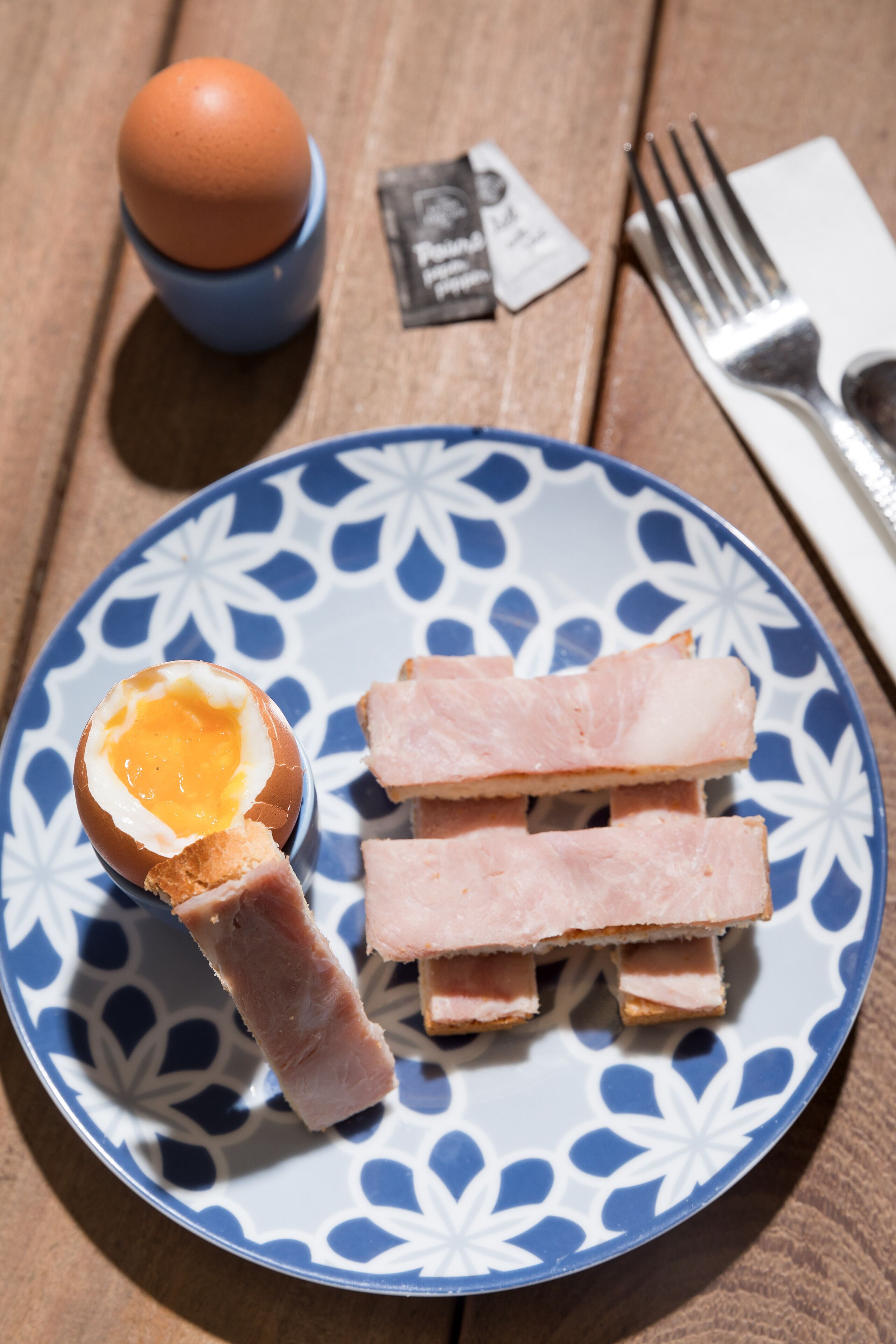 Een bord met een gekookt ei en plakjes ham, op een bord met blauw-witte patronen.