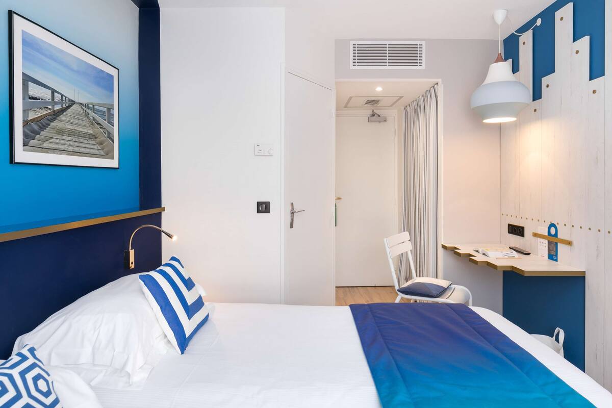 A hotel room with a bed, a desk, a chair, a shower, and a bathroom.