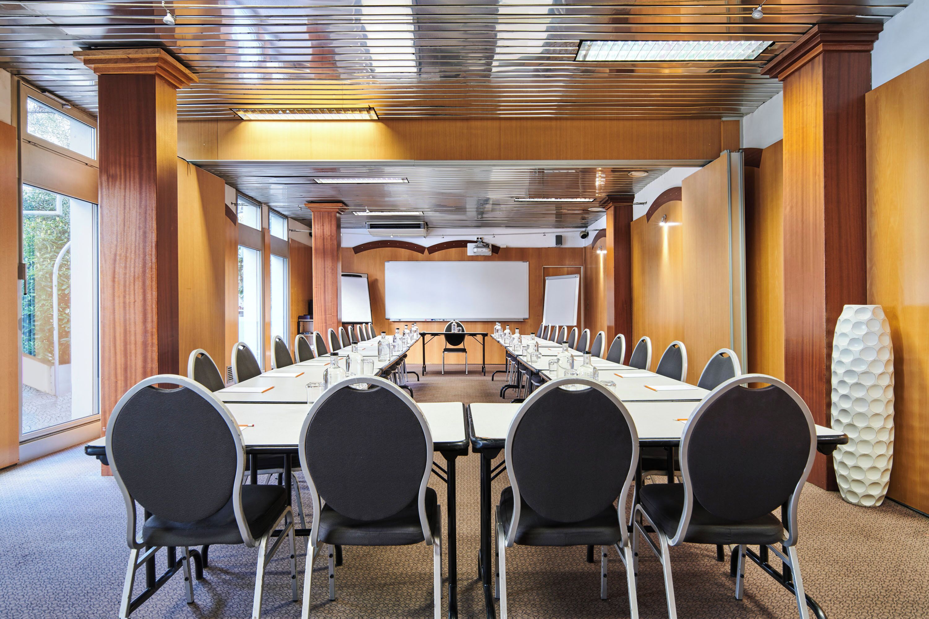 Una sala de conferencias con una larga mesa, sillas, una pantalla para proyector y una pizarra.