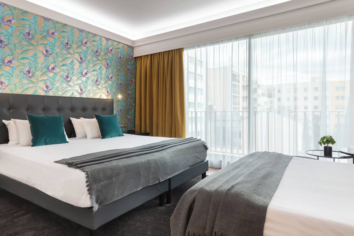Une chambre d’hôtel moderne avec un grand lit, une tête de lit, une fenêtre avec des rideaux et une vue sur la ville.