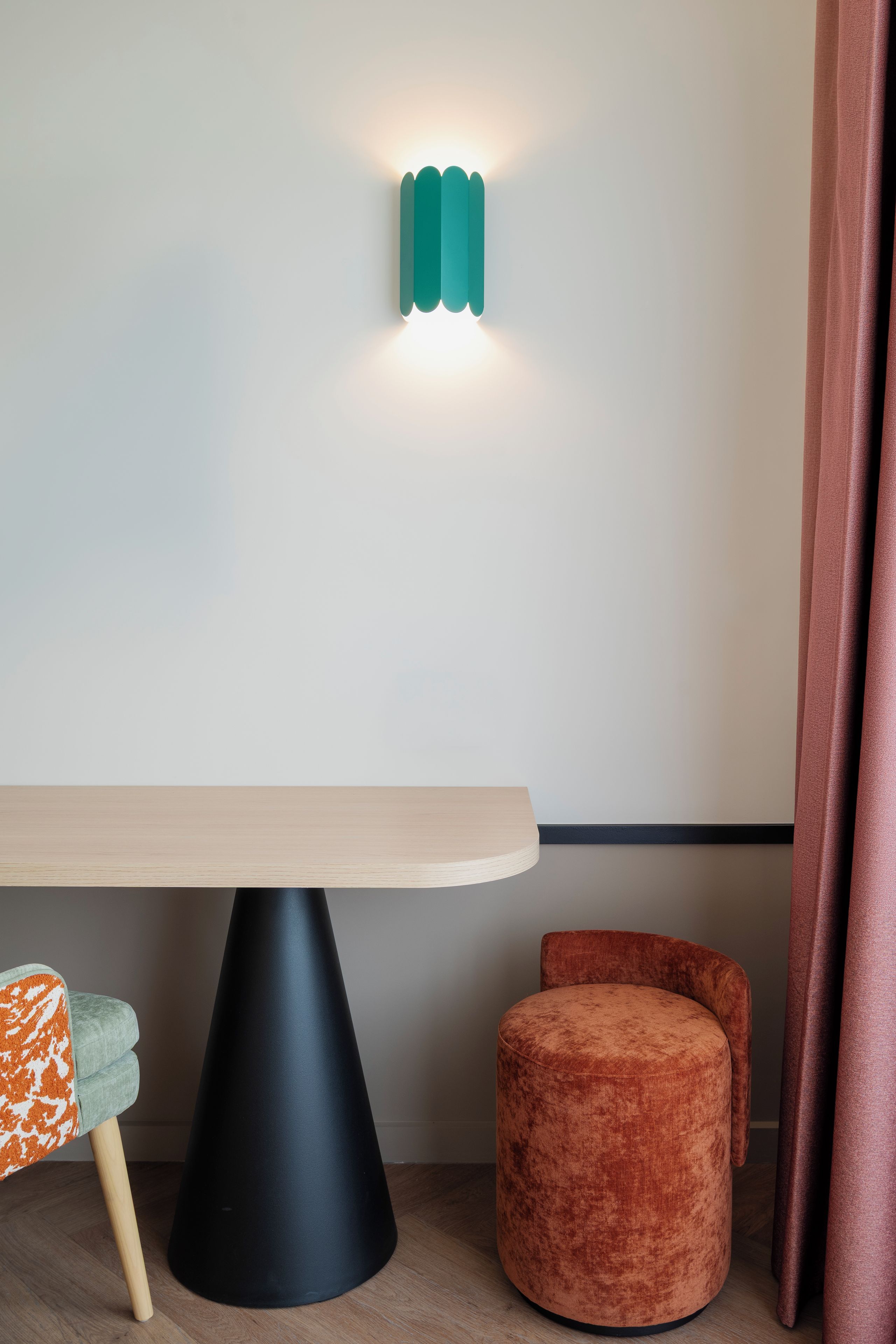 Un interior moderno con una mesa de madera, base negra con forma de cono, silla con estampado naranja y blanco, y un otomano redondo naranja.