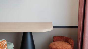 Un interior moderno con una mesa de madera, base negra con forma de cono, silla con estampado naranja y blanco, y un otomano redondo naranja.