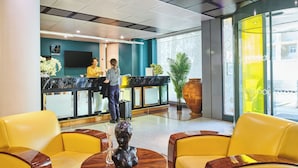 A reception area with a counter, two receptionists, yellow chairs, a wooden table with a sculpture, and a large potted plant. - Hotel Charlemagne By HappyCulture  (Lyon)