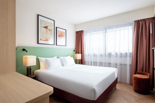 Habitación de hotel con una cama grande, dos mesitas de noche, un escritorio y una silla. Hay dos cuadros enmarcados en la pared.