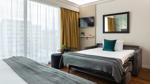 A modern hotel room with a large bed, a flat-screen TV, a small table with a plant, and a window with sheer curtains. - Hotel Charlemagne By HappyCulture  (Lyon)