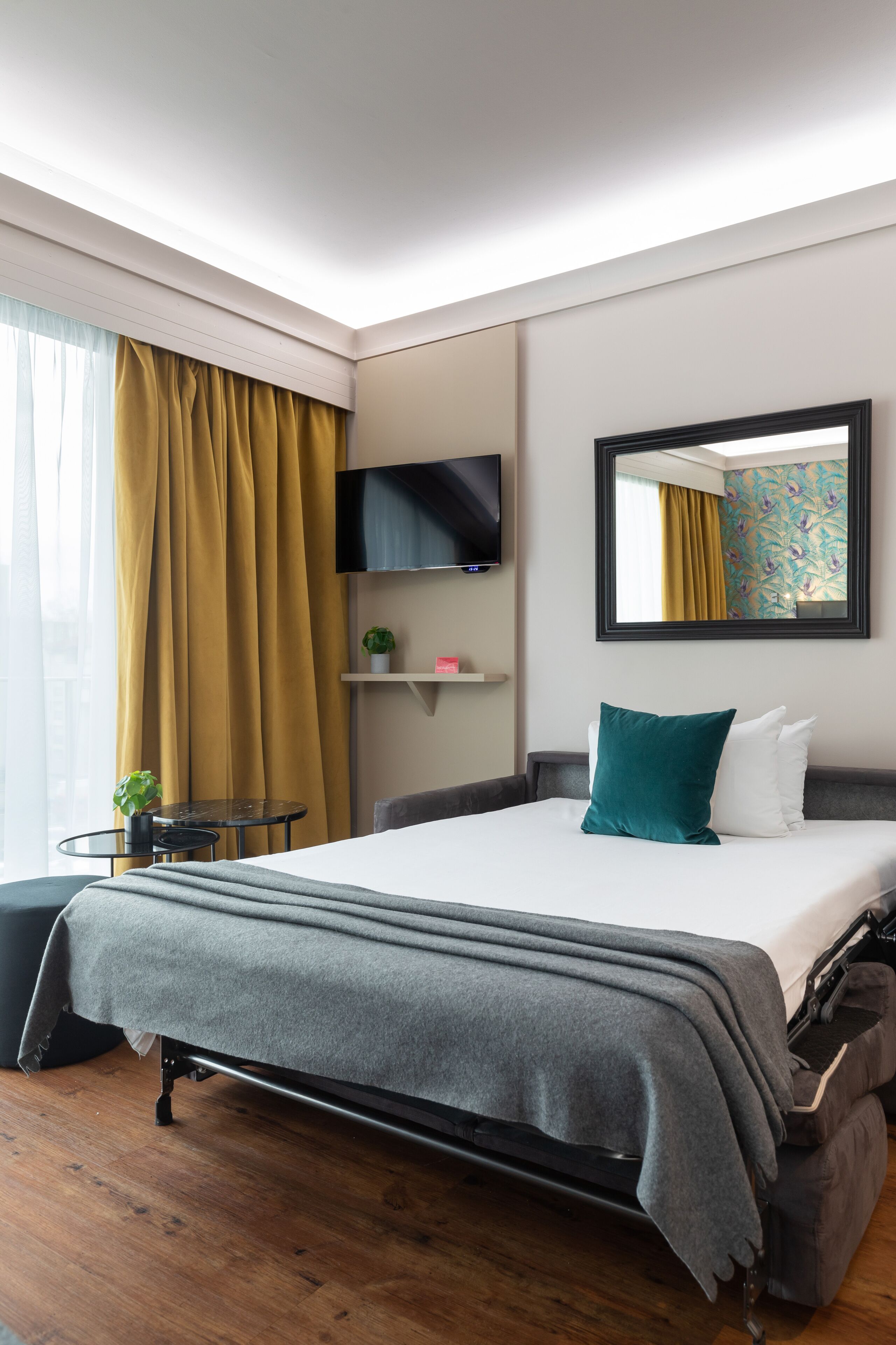 Une chambre d’hôtel moderne avec un grand lit, un téléviseur à écran plat, une petite table avec une plante et une fenêtre avec des rideaux.