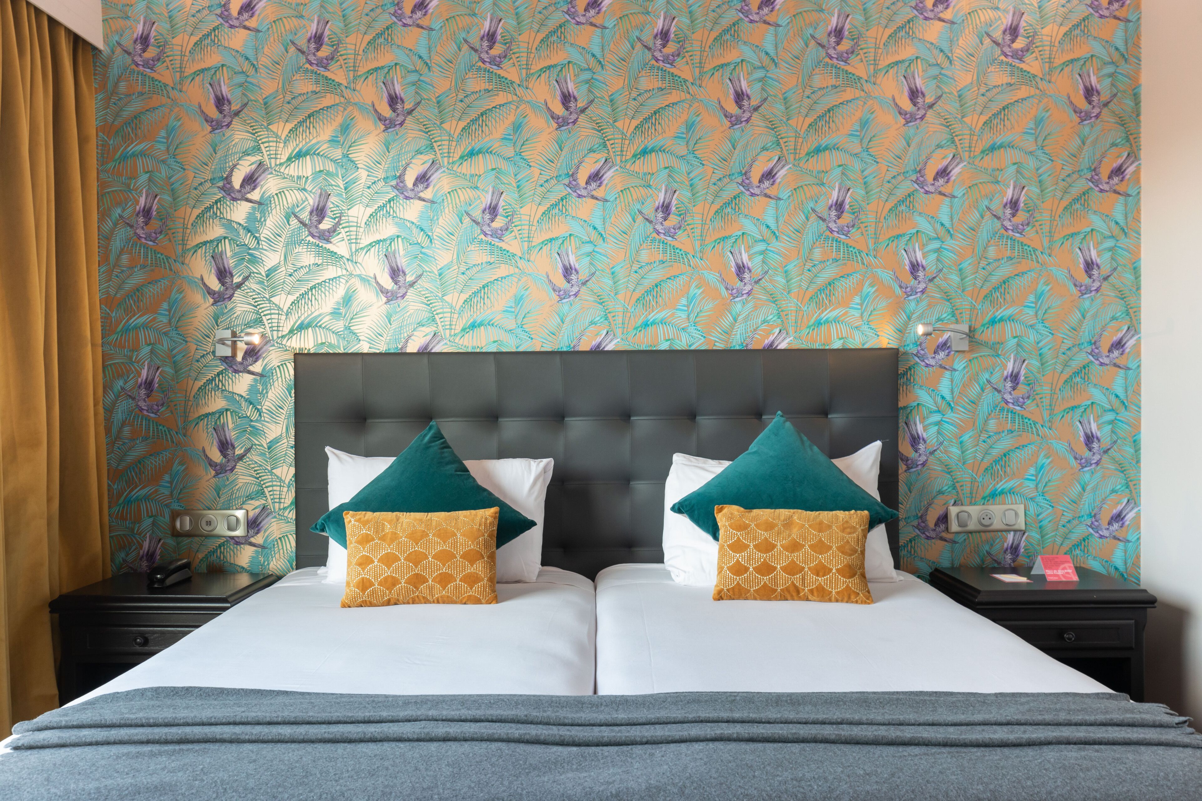 A double bed with a tufted headboard, two nightstands, and patterned wallpaper.