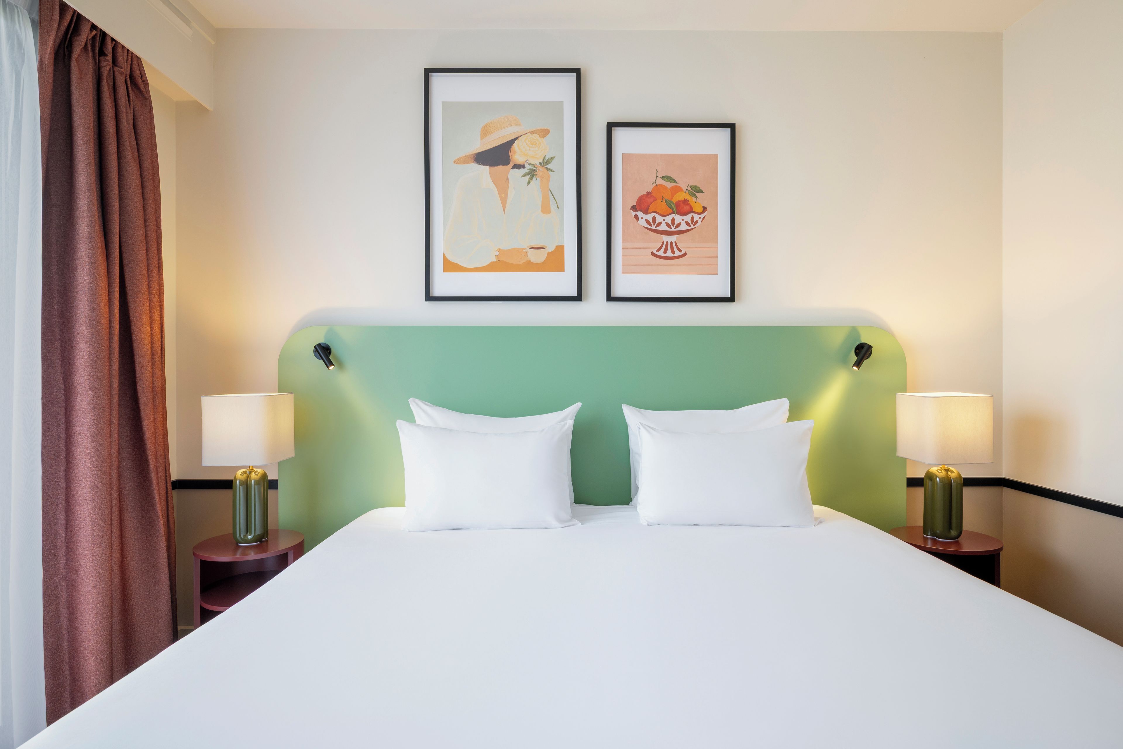 A hotel room with a bed, two nightstands, a green headboard, and two framed pictures on the wall.