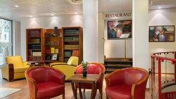 Une bibliothèque avec des étagères, un fauteuil rouge et jaune, une petite table avec une plante, et un panneau indiquant un restaurant.