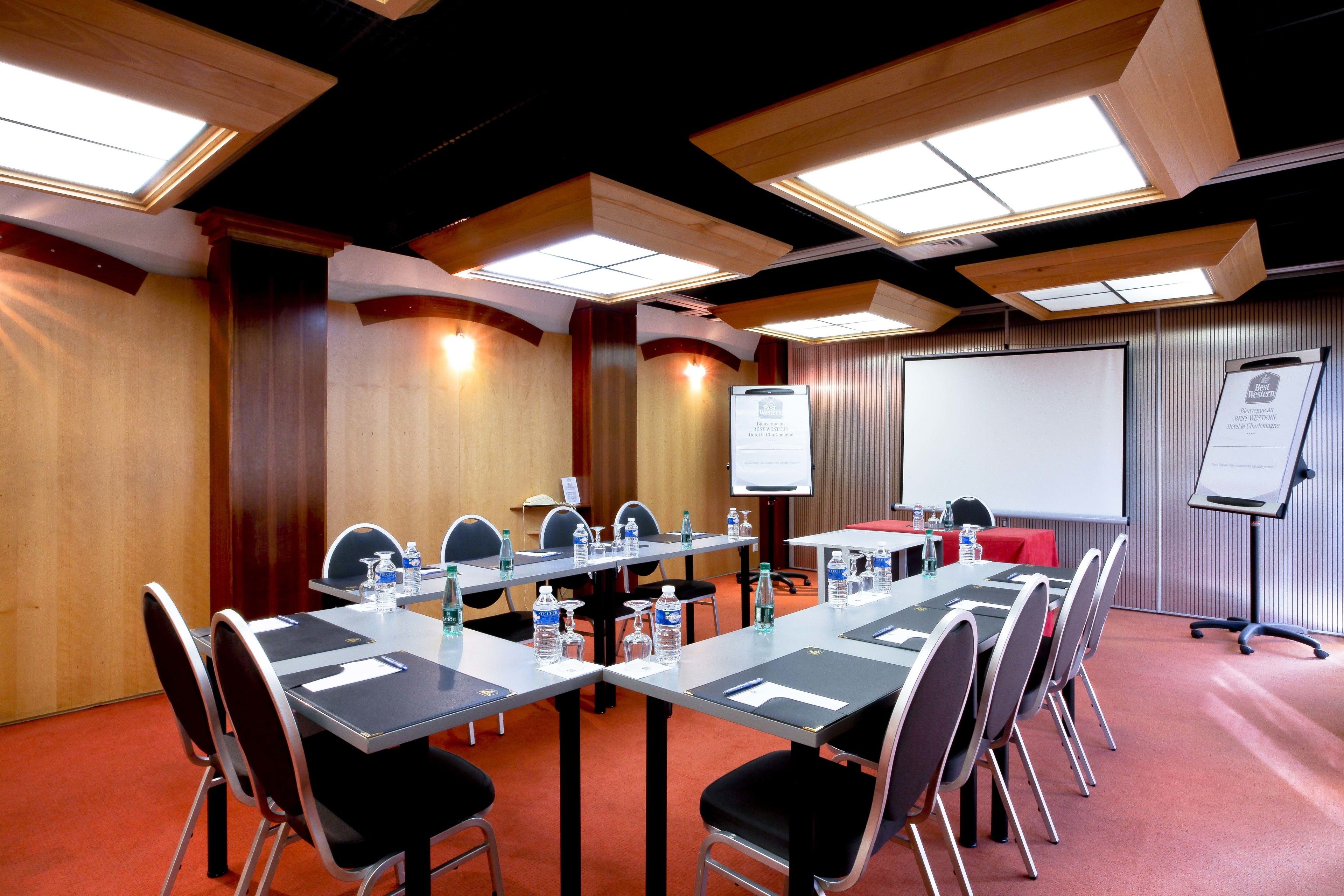 Un salón de conferencias con una larga mesa, sillas, una pantalla de proyector y una pizarra.