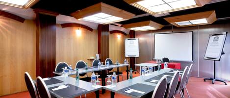 Un salón de conferencias con una larga mesa, sillas, una pantalla de proyector y una pizarra.