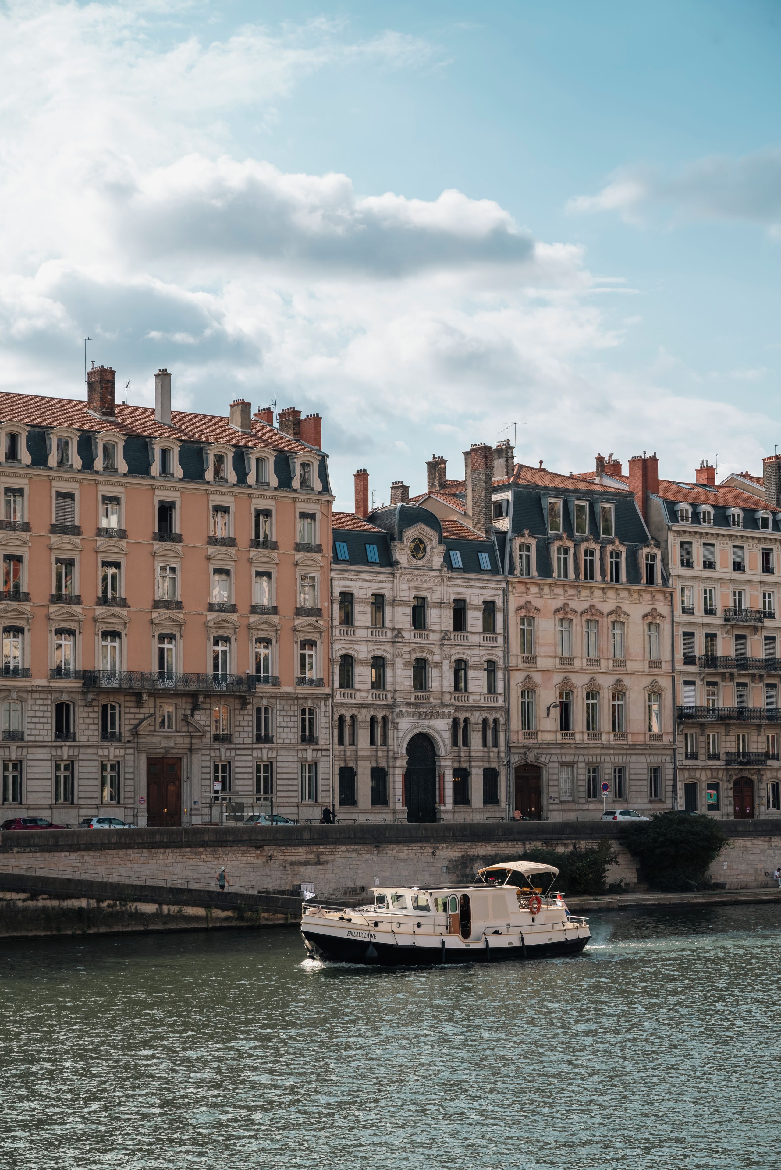 Ein historisches Gebäude mit mehreren Stockwerken und klassischer Architektur, im Vordergrund fließt ein Fluss.