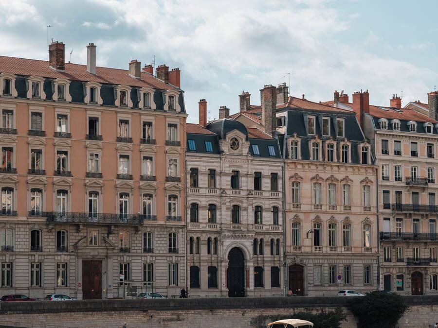 Um edifício histórico com vários andares, arquitetura clássica e um rio ao primeiro plano.
