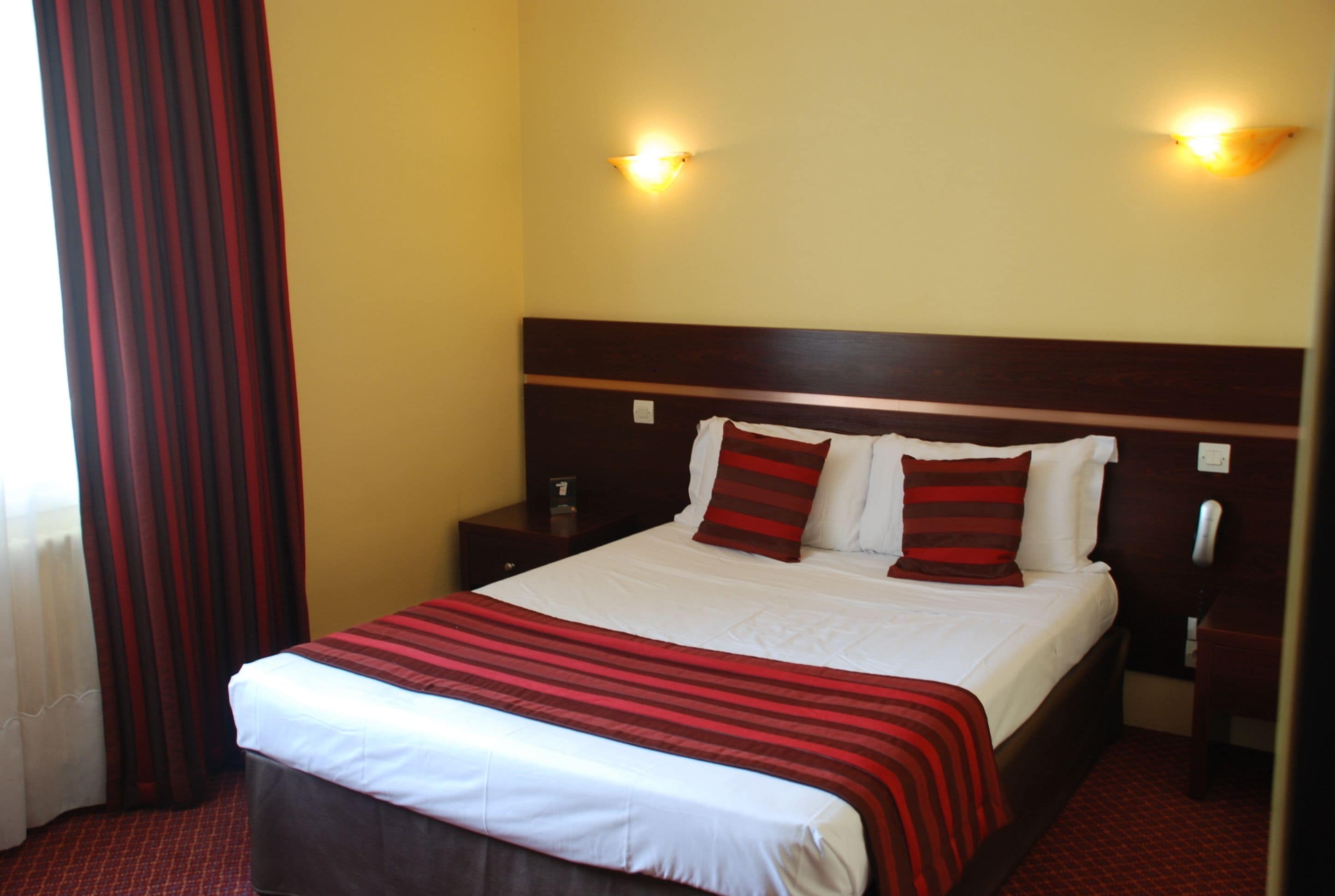 A neatly made bed with a striped bedspread, two bedside tables with lamps, and a curtain on the window.
