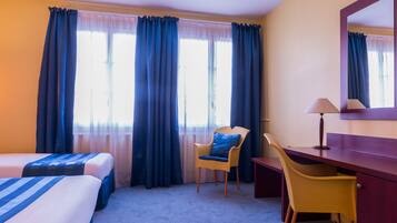 A hotel room with two beds, a desk, a chair, and a large window with curtains.