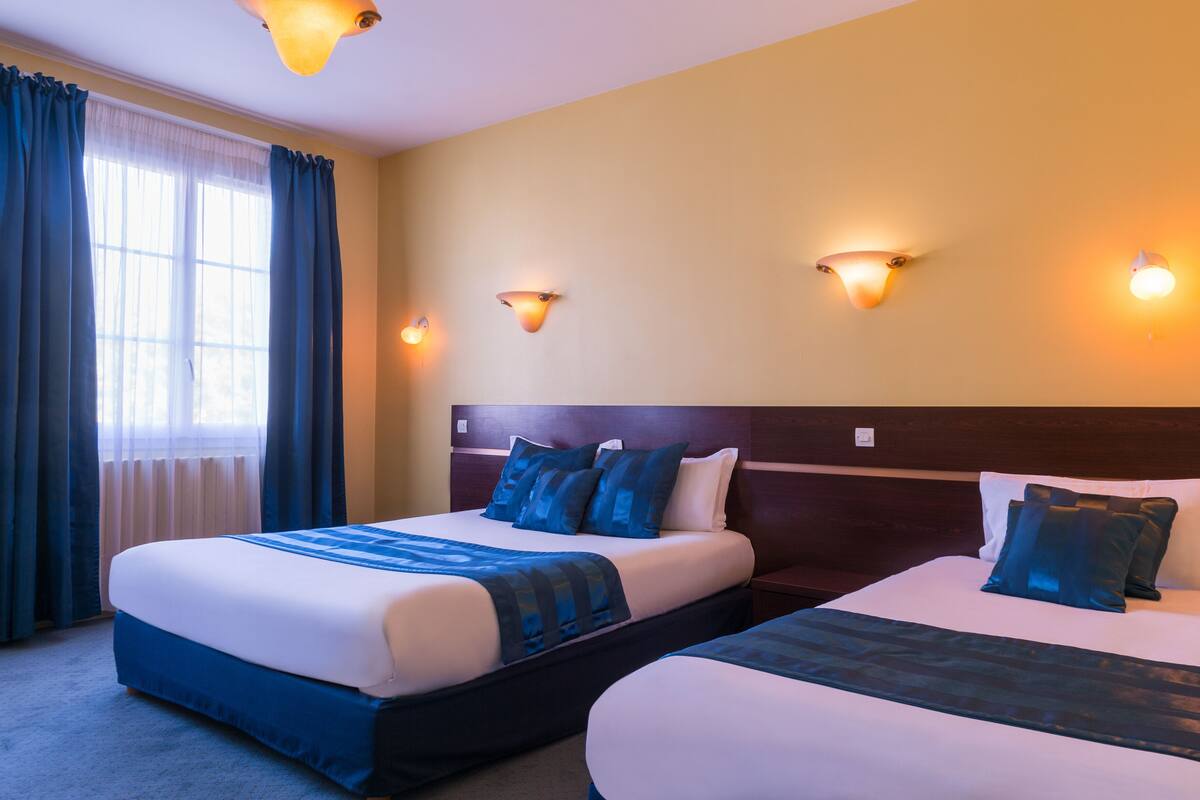 Ein Hotelzimmer mit zwei Betten, einem großen Fenster mit Vorhängen und Wandleuchten.