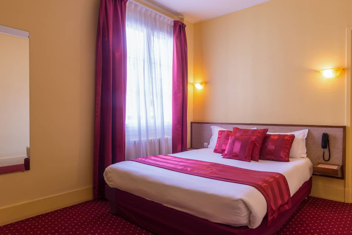 Ein Hotelzimmer mit einem großen Bett, einem Nachttisch, einem Telefon und einem Fenster mit Vorhängen.