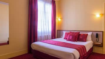 Habitación de hotel con una cama grande, una mesita de noche, un teléfono y una ventana con cortinas.