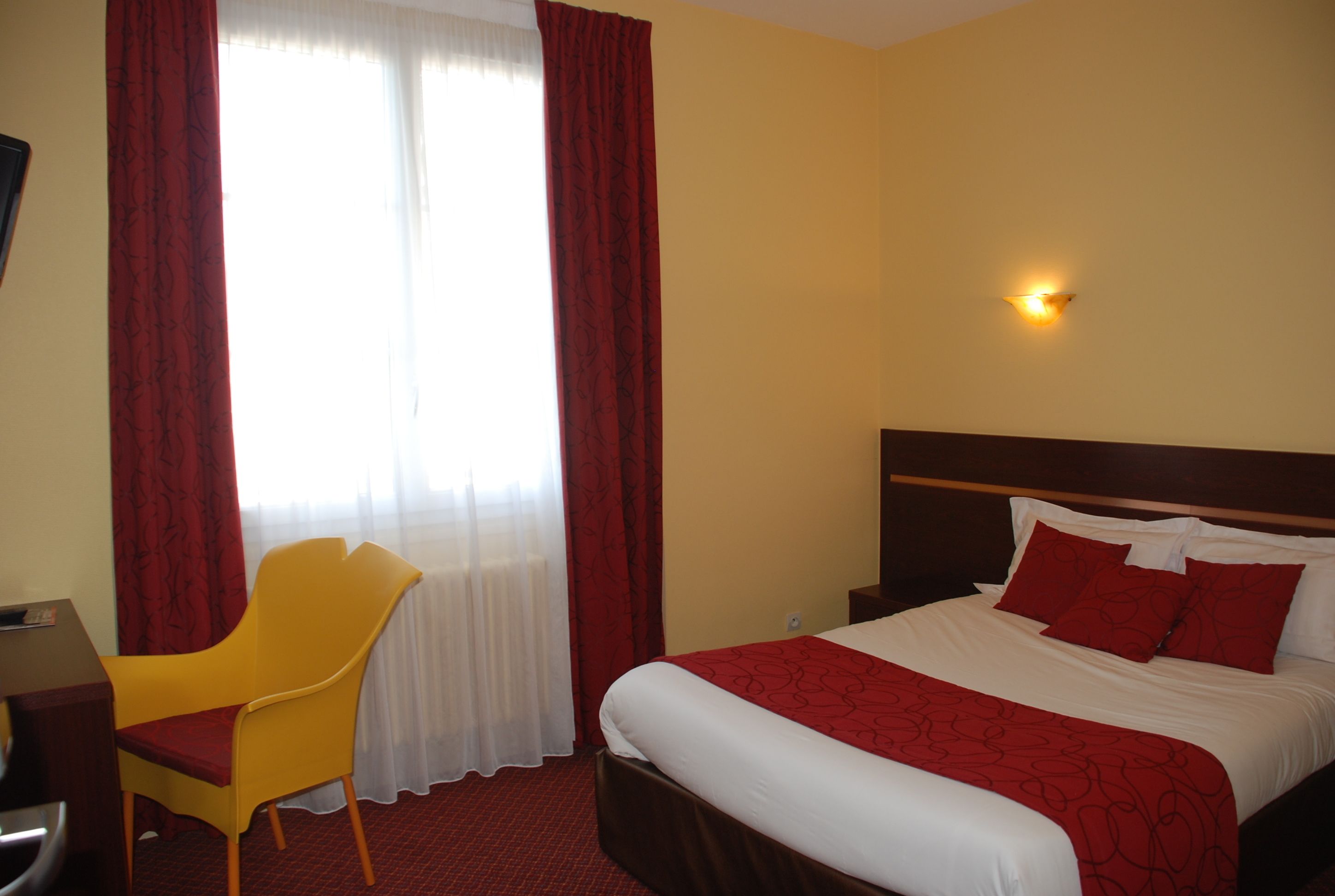 Ein Hotelzimmer mit Bett, Stuhl, Schreibtisch und einem fensterbepflanzten Fenster.
