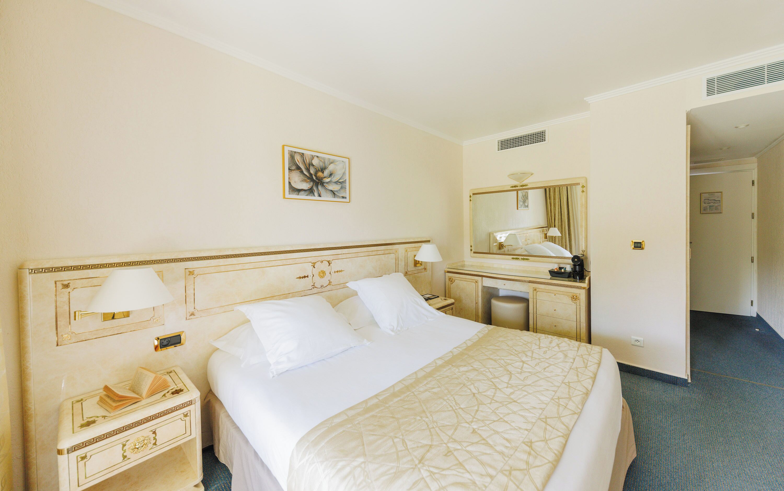 A hotel room with a large bed, bedside tables, a mirror, and a door leading to another room.
