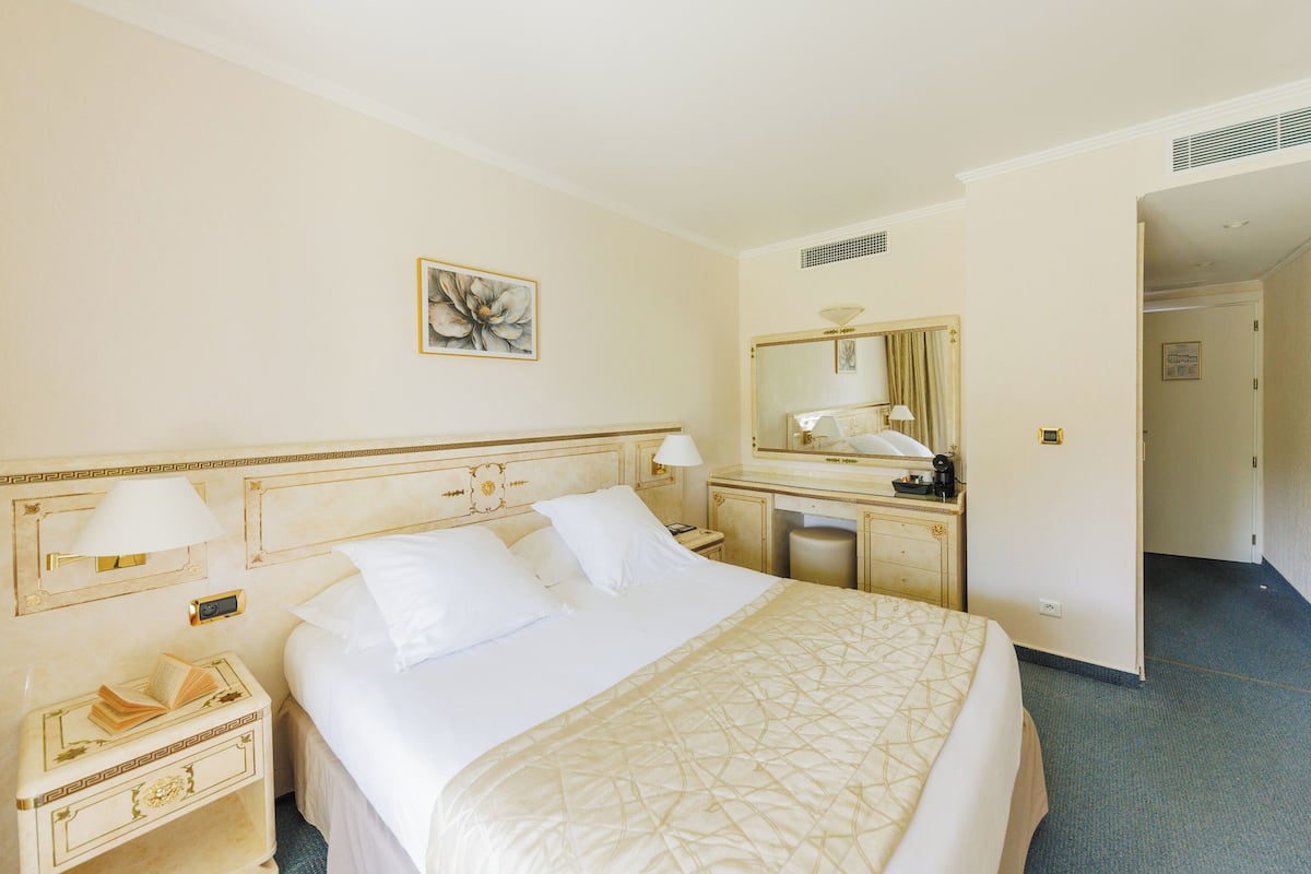 A hotel room with a large bed, bedside tables, a mirror, and a painting on the wall.