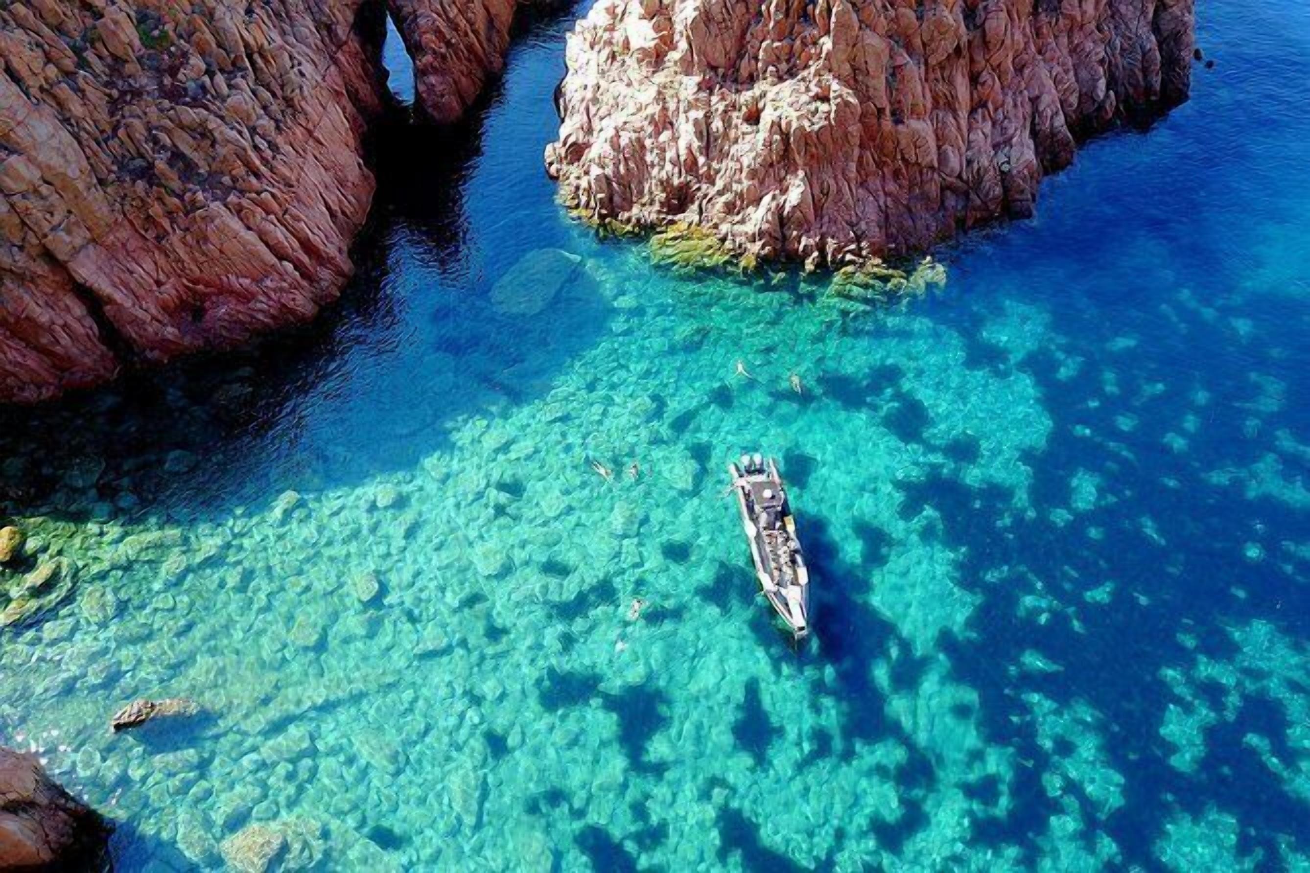 A boat in clear blue waters near rocky formations.