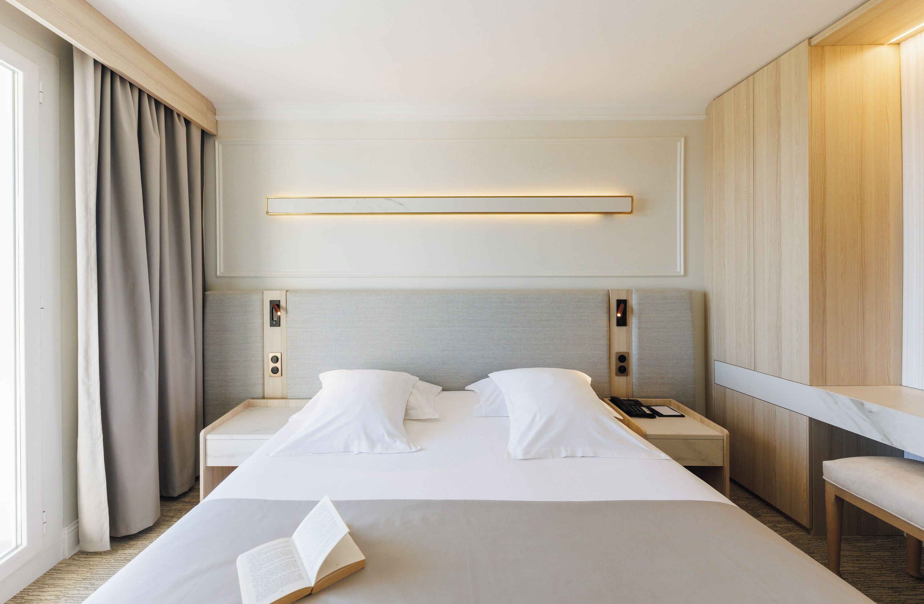Una habitación de hotel con una cama grande, mesitas de noche, una lámpara de lectura y vistas al exterior.
