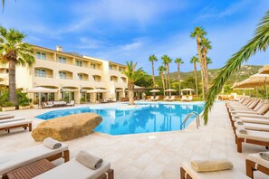 A poolside area with lounge chairs, a large rock, and a building with multiple balconies.