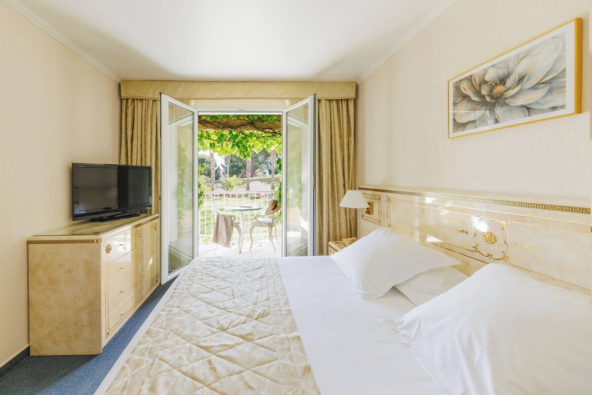A hotel room with a bed, a TV on a cabinet, and a view of the outdoors.