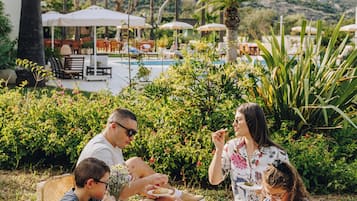 Enjoy a meal al fresco with family in a lush tropical setting, surrounded by a pool and palm trees.