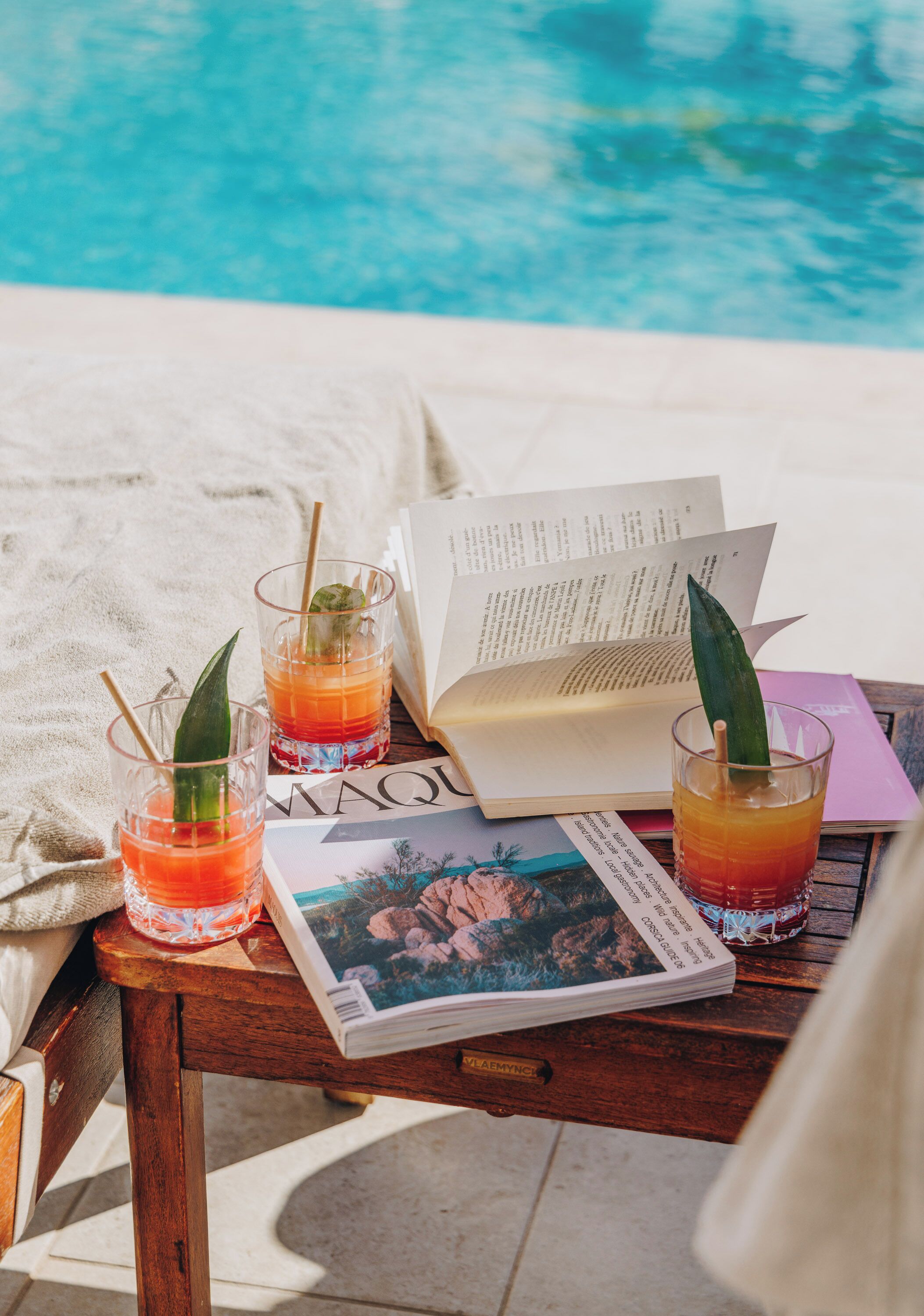 A wooden table with two glasses of drink, a book, and a magazine.