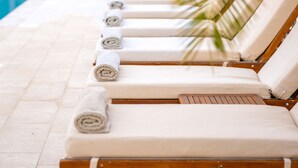 A row of sun loungers with towels, a pool, and palm trees in the background. - Hotel Corsica & Spa Serena (Calvi)