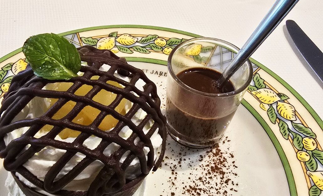 A dessert with a lattice on top, a mint leaf garnish, and a glass of chocolate sauce with a spoon.