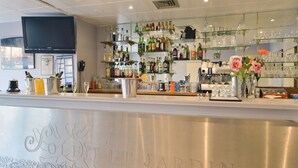 Eine Bar mit einer polierten Theke, Regalen voller Spirituosenflaschen und einem an der Wand befestigten Fernseher.