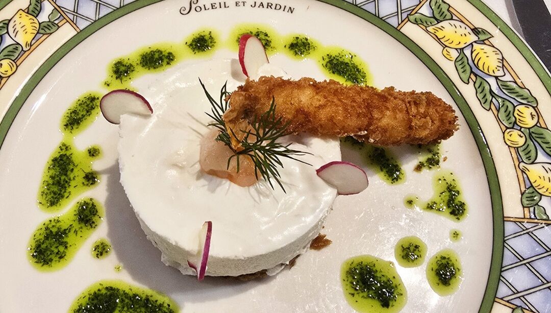 A plate of food with a fried item, a creamy base, and green garnish.