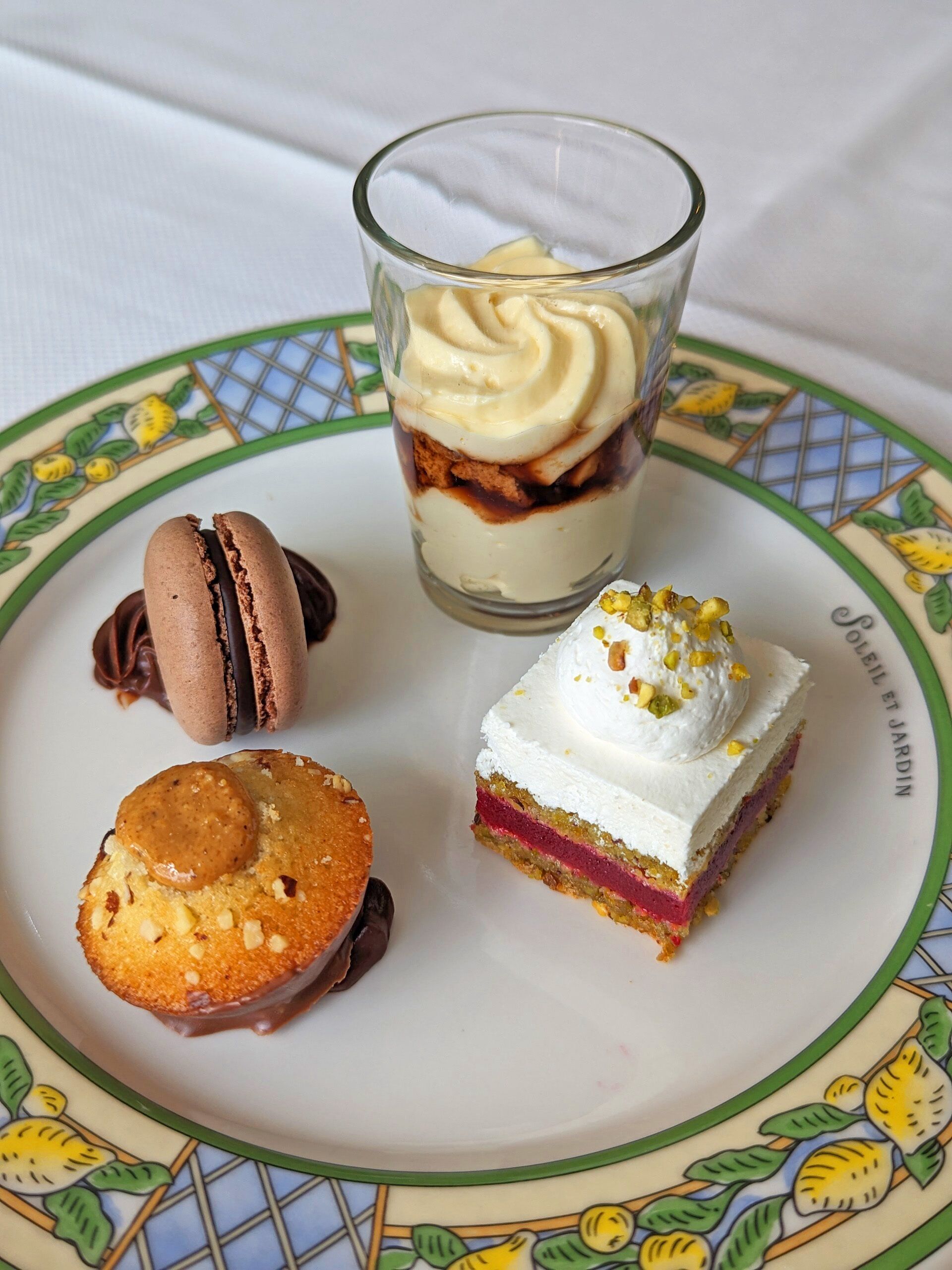 A dessert plate with macarons, a layered dessert in a glass, and a square cake with whipped cream.