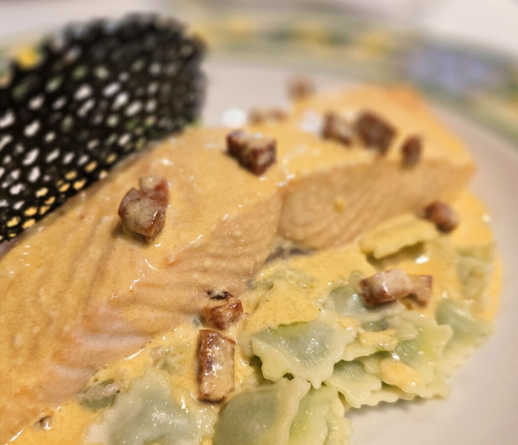 A close-up of a dish with salmon and a creamy sauce, accompanied by a black textured item.