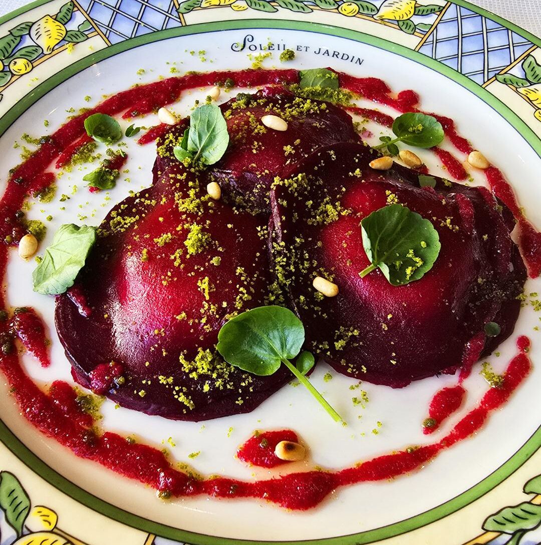 Un plato de comida con rodajas de remolacha, adornado con hojas verdes y nueces, sobre un plato decorativo con estampado floral.