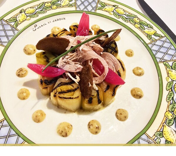A plate of food with grilled vegetables and meat, garnished with herbs and a decorative plate design.