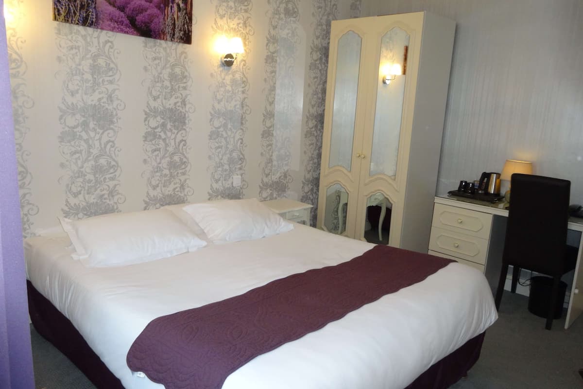 A neatly made bed with a white and maroon bedspread, a dresser with a mirror, and a desk with a lamp.
