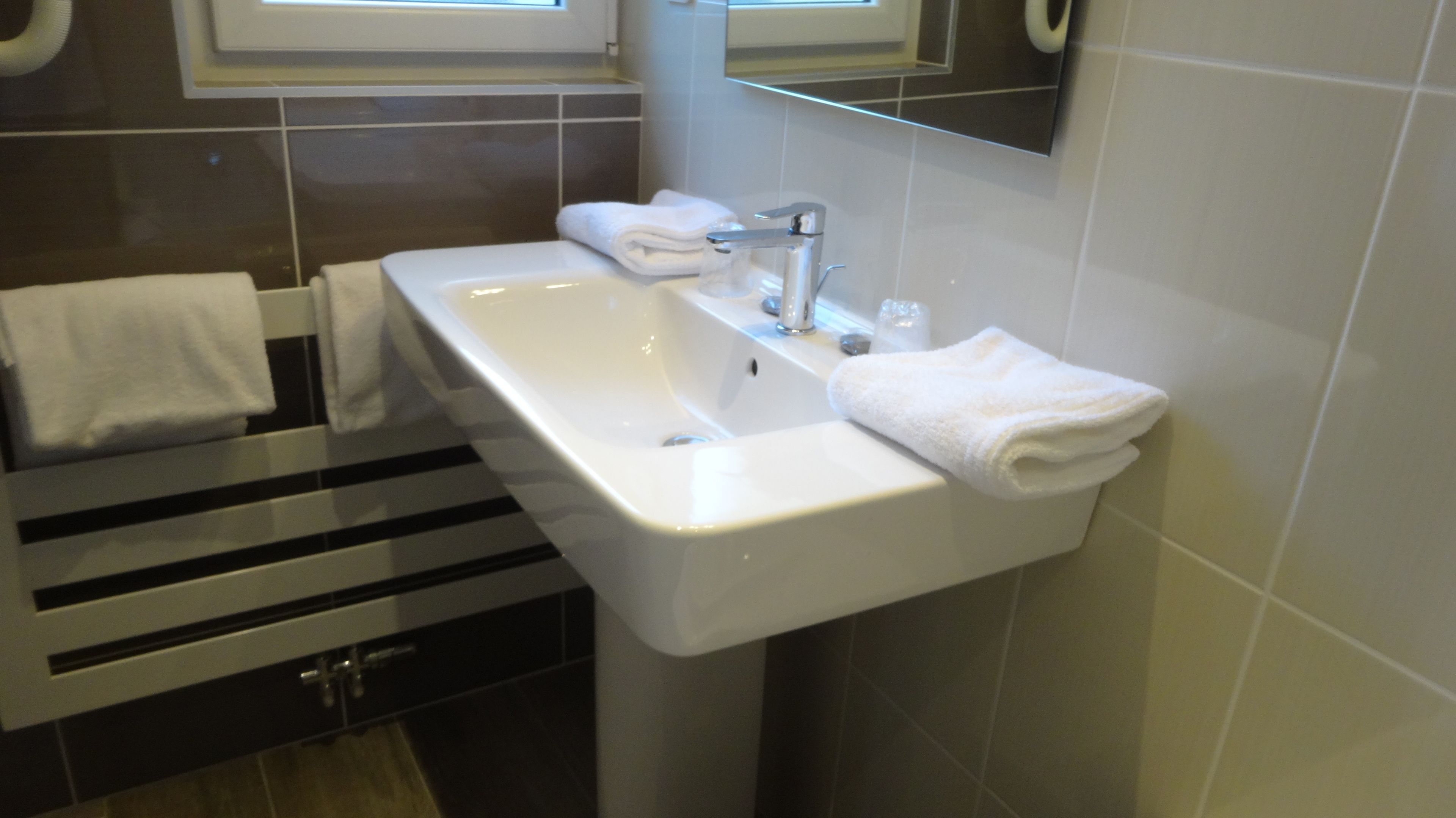 A bathroom with a white sink, a mirror above it, and a towel rack with two towels.