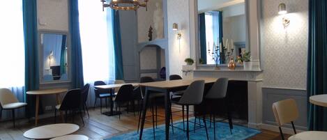 A dining area with a large table, multiple chairs, a chandelier, and a fireplace with a mirror above it.