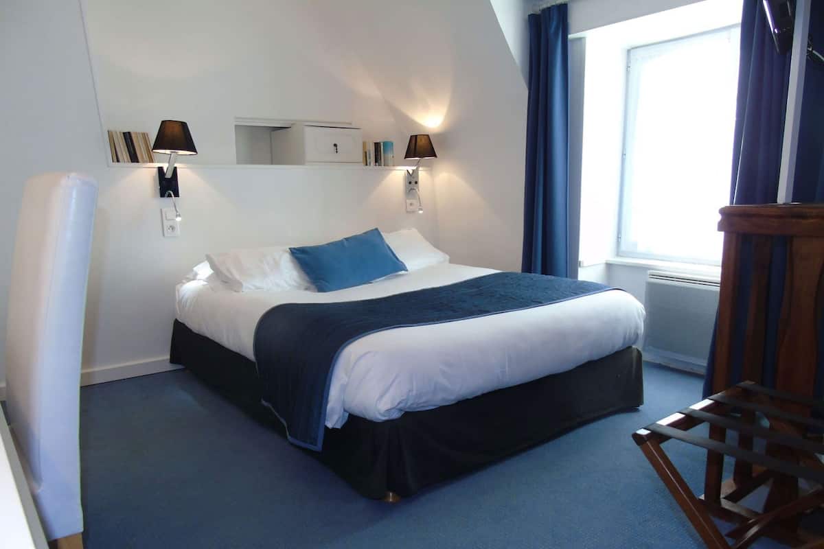 A neatly made bed with a dark headboard, two bedside lamps, a blue blanket, and a wooden chair.