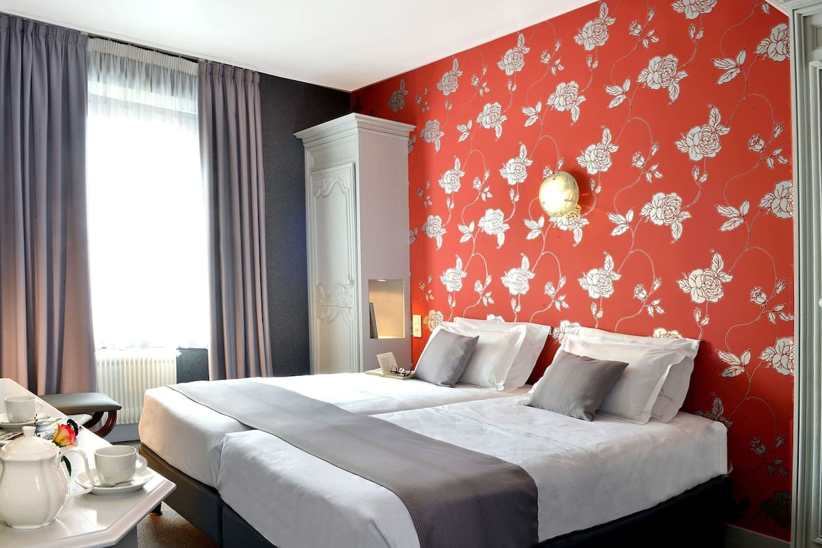 A hotel room with a large bed, a nightstand, a lamp, and a window with curtains.