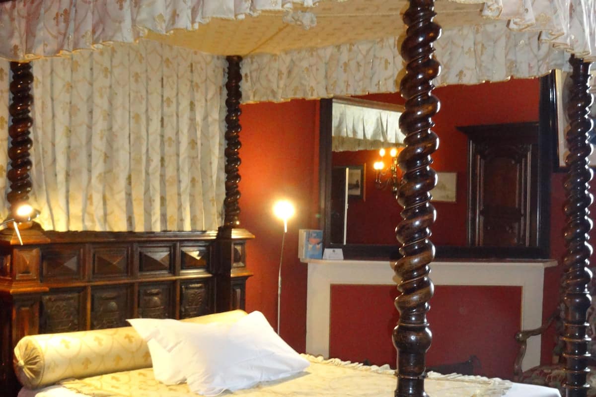 A four-poster canopy bed with white linens and a wooden frame.
