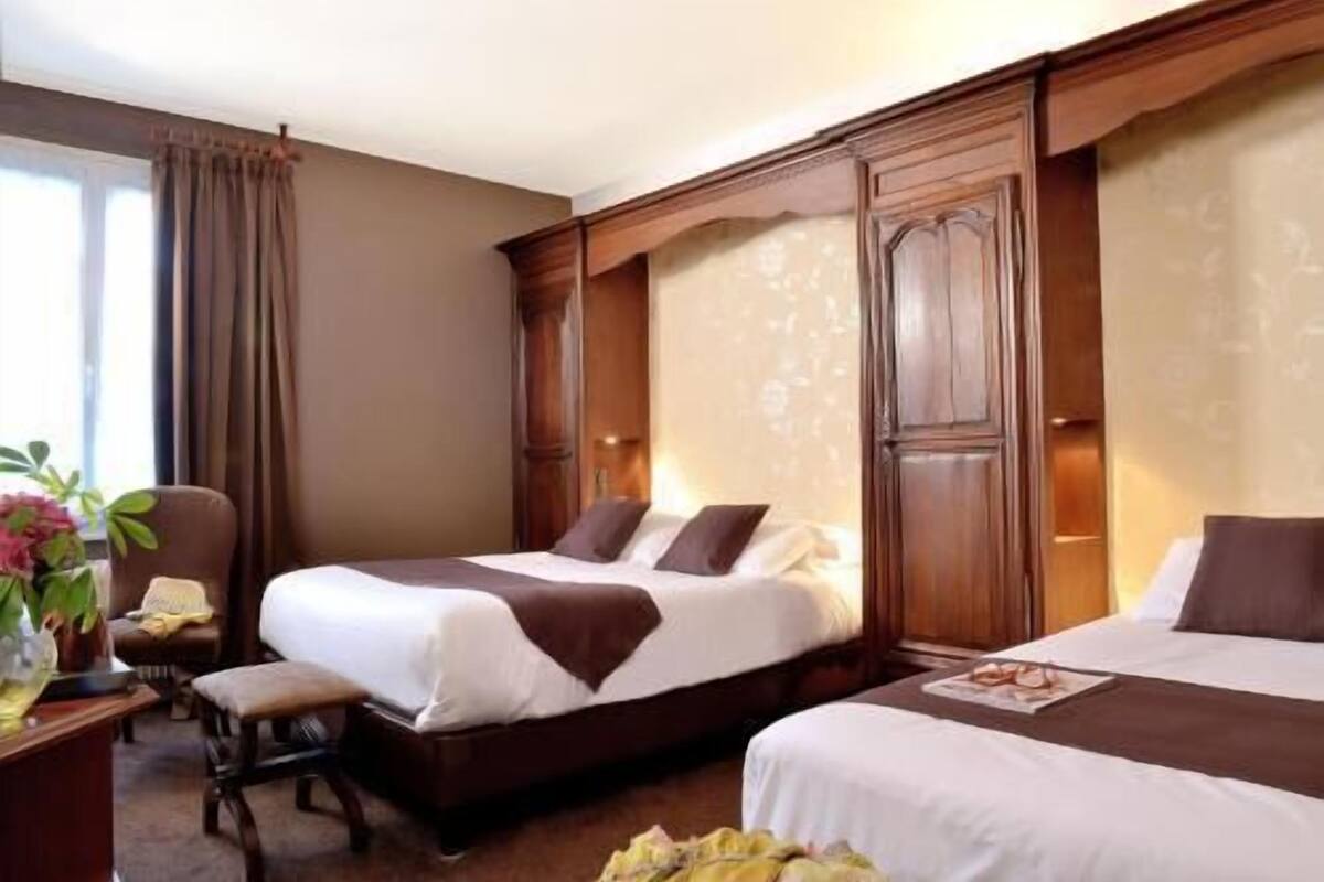 A hotel room with two beds, a desk, a chair, and a window with curtains.