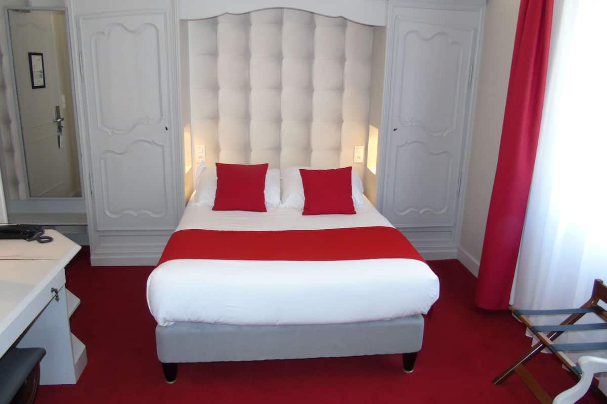 A hotel room with a large bed, white headboard, red accents, and a red carpet.