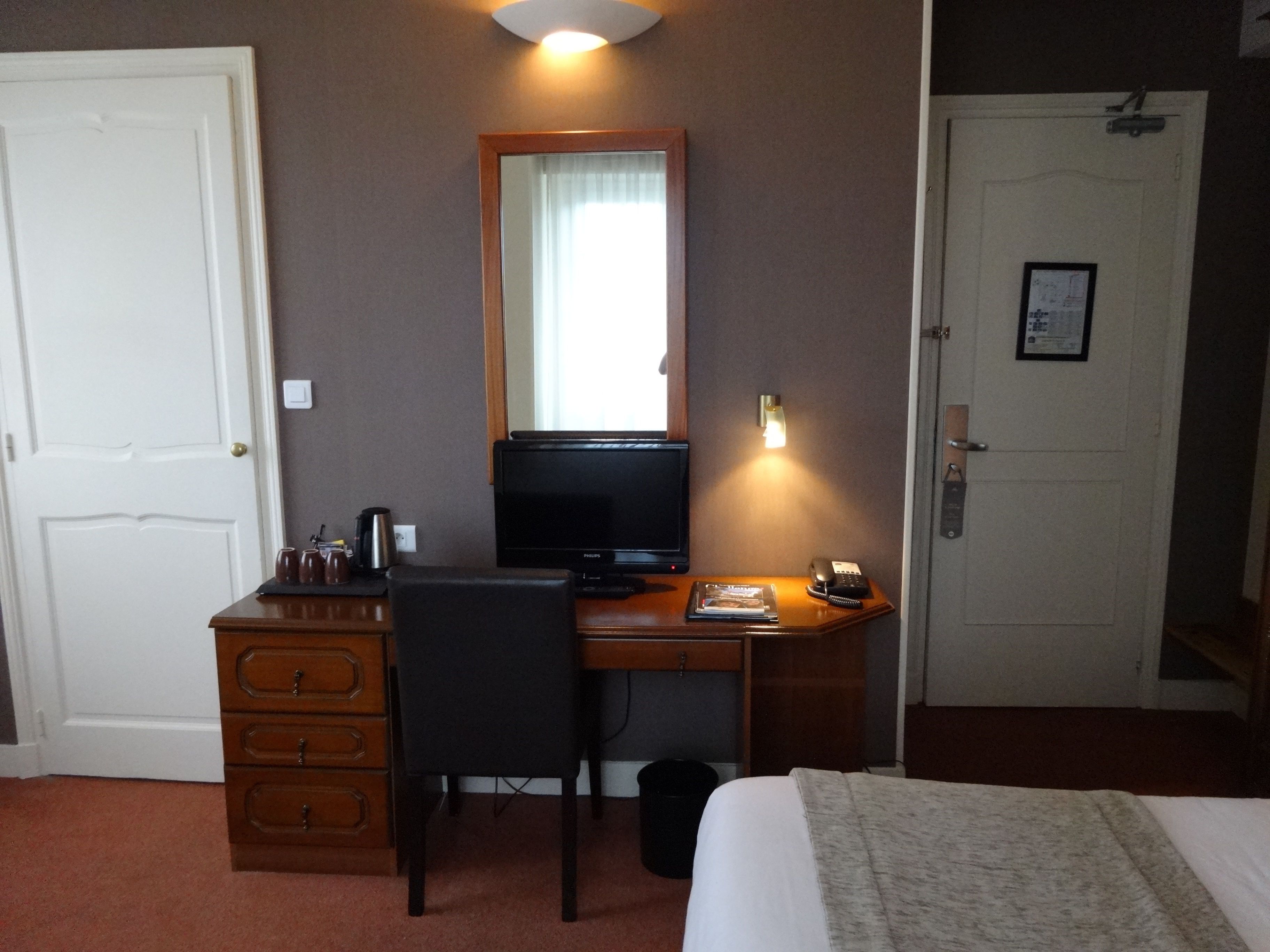 A hotel room with a wooden desk, a television, a telephone, and a bed.